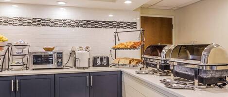 A modern kitchen with a buffet setup, including a toaster, a bread rack, and a grill station.