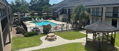 Um pátio com piscina, espreguiçadeiras, um gazebo e um pequeno jardim.