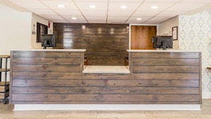 Un comptoir d’accueil avec un revêtement en bois, un plafond carrelé doté d’un éclairage encastré et un mur orné d’un motif décoratif sur le côté droit.