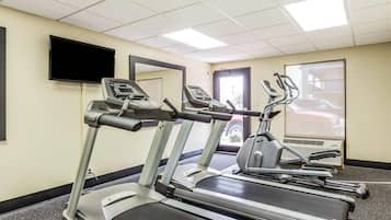 Et fitnessrum med løbebånd, et fjernsyn og en dør, der fører udendørs.