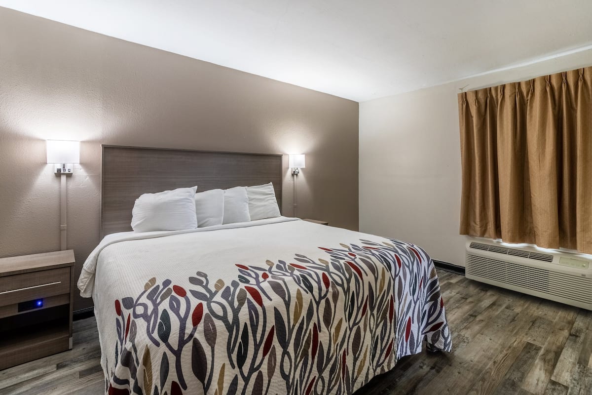 A hotel room with a bed, two wall-mounted lights, a heater, and a window with curtains.