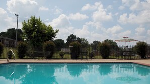 A swimming pool with a clear blue water surface, surrounded by a fence, trees, and outdoor furniture. - Red Roof Inn & Suites Jackson, TN (Jackson)
