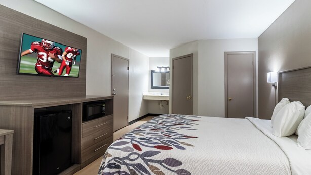 A hotel room with a bed, a TV mounted on the wall, a microwave, a small desk, and a wardrobe. - Red Roof Inn & Suites Jackson, TN (Jackson)
