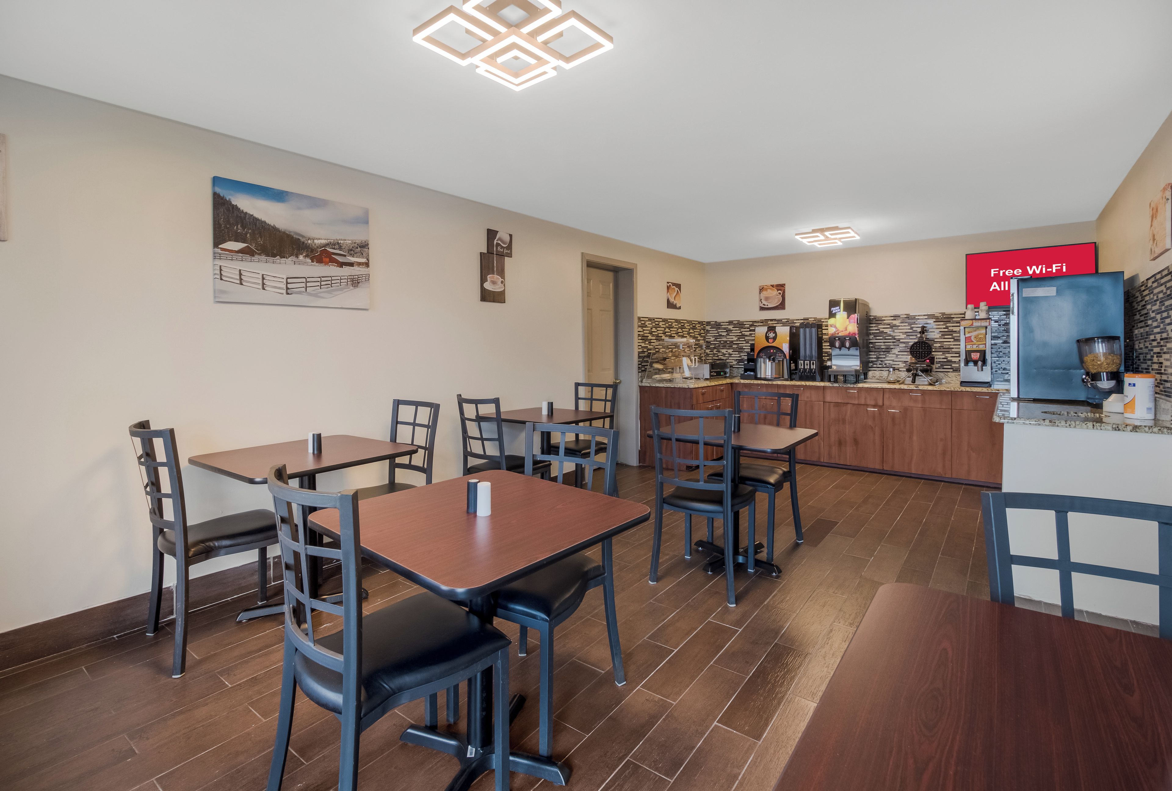 A dining area with tables and chairs, a kitchen with coffee machines, and a sign offering free Wi-Fi.