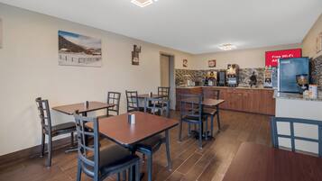 A dining area with tables and chairs, a kitchen with coffee machines, and a sign offering free Wi-Fi.