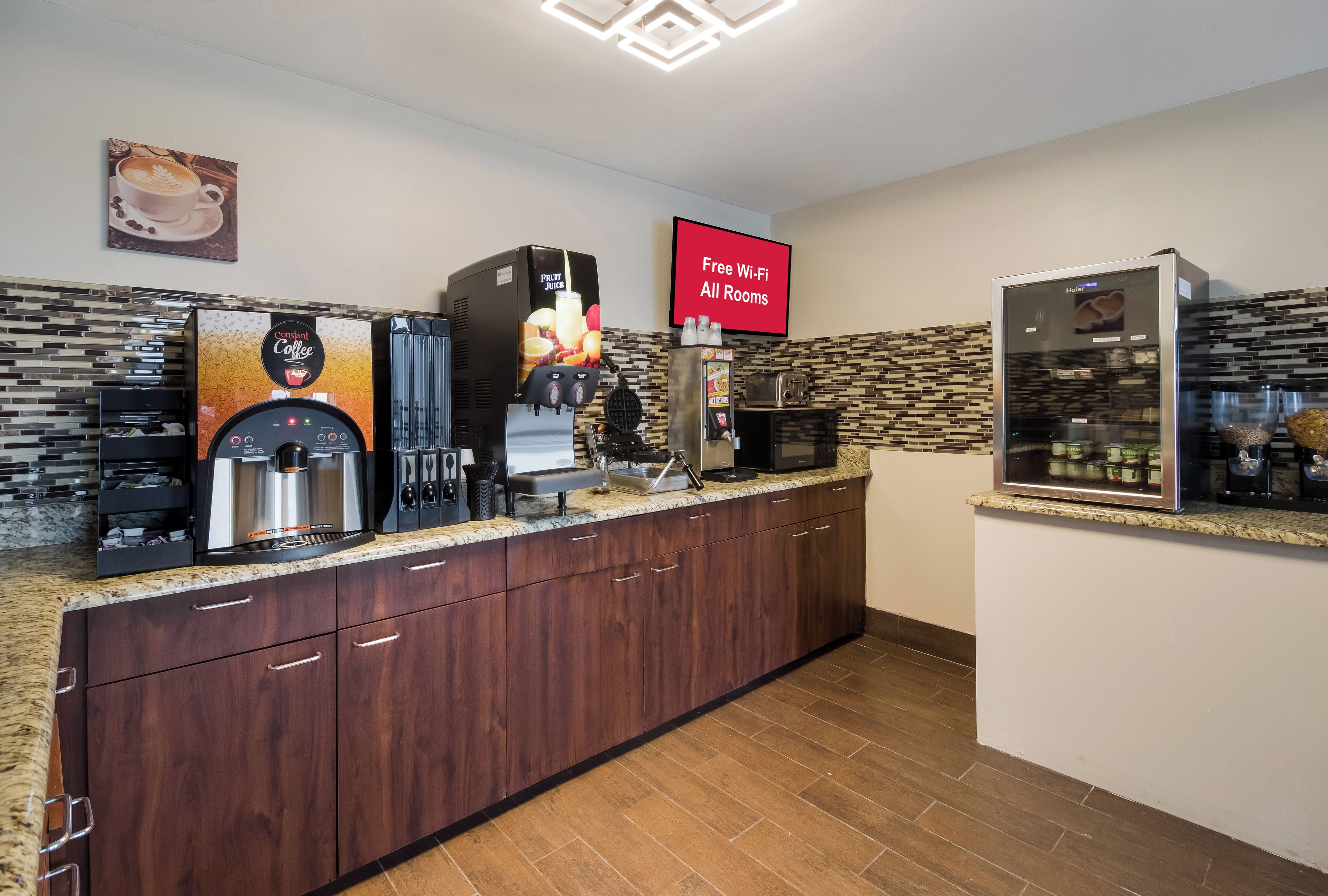 A modern coffee station with multiple coffee machines, a fruit juice dispenser, and a refrigerator.