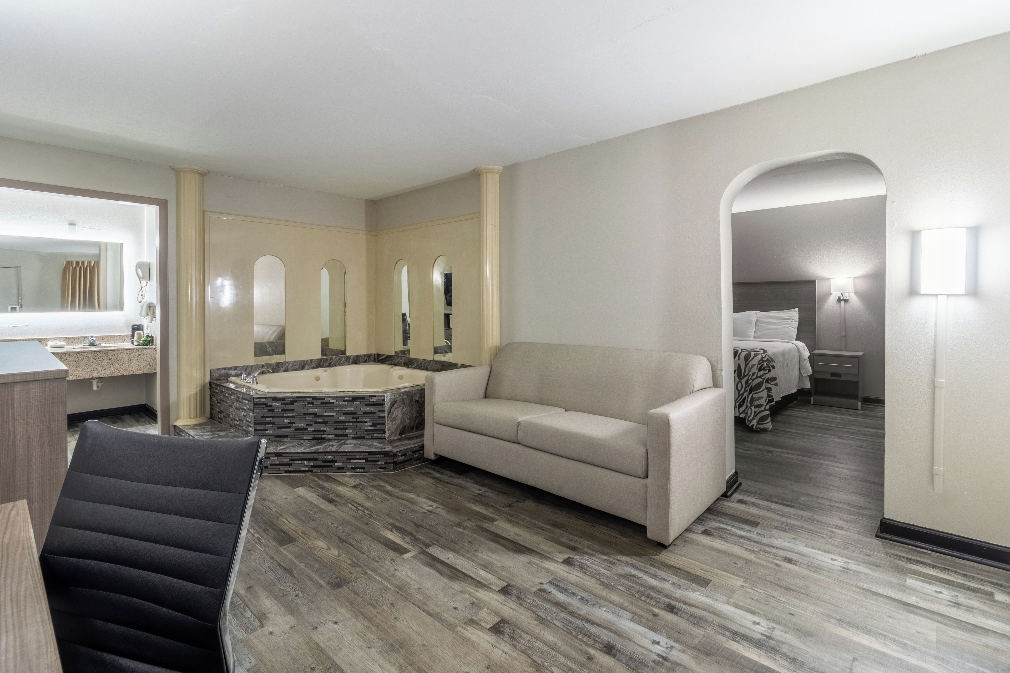 A hotel room with a sofa, a bathtub, a mirror, and a bed.