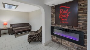 Ein modernes Wohnzimmer mit Kamin, einer Couch, einer Bank und einem an der Wand befestigten Schild für Red Roof Inn Suites.