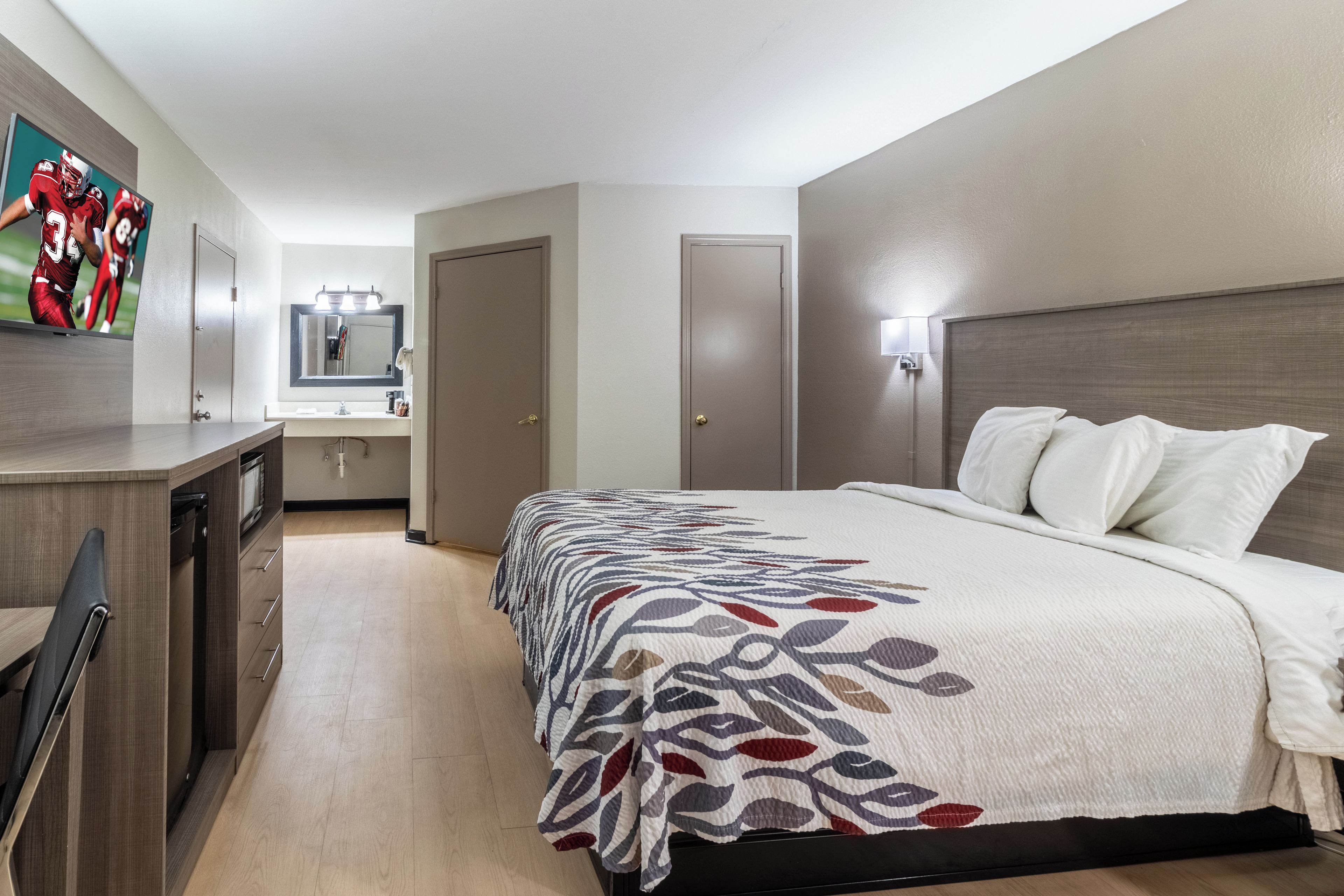 A hotel room with a bed, a desk, a mirror, and a television.