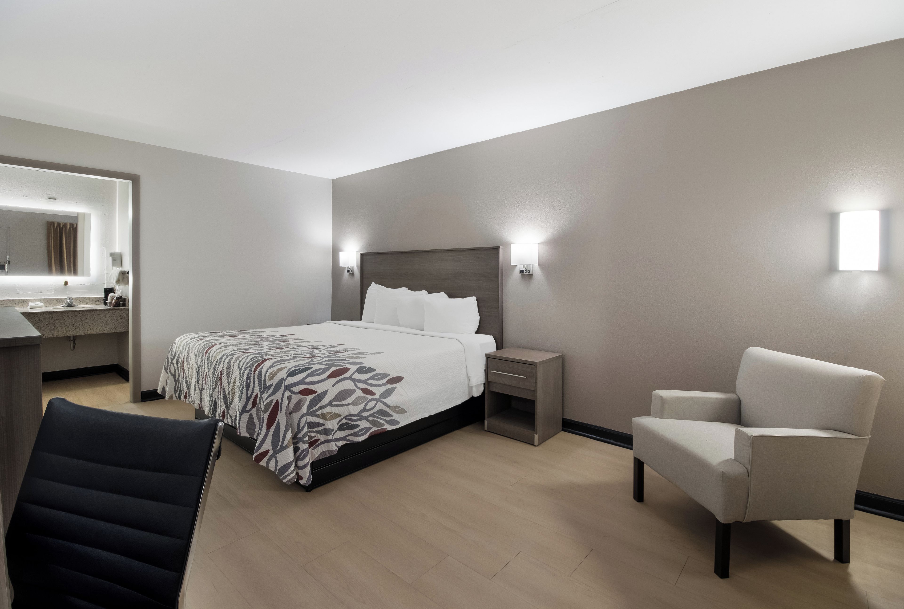 A hotel room with a bed, a chair, a nightstand, a desk, and a mirror.