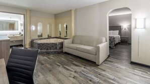 Ein modernes Hotelzimmer mit einem großen Bett, einer Couch, einem kleinen Tisch, einem Sessel und einem Badezimmer mit einer Badewanne und einem Spiegel.