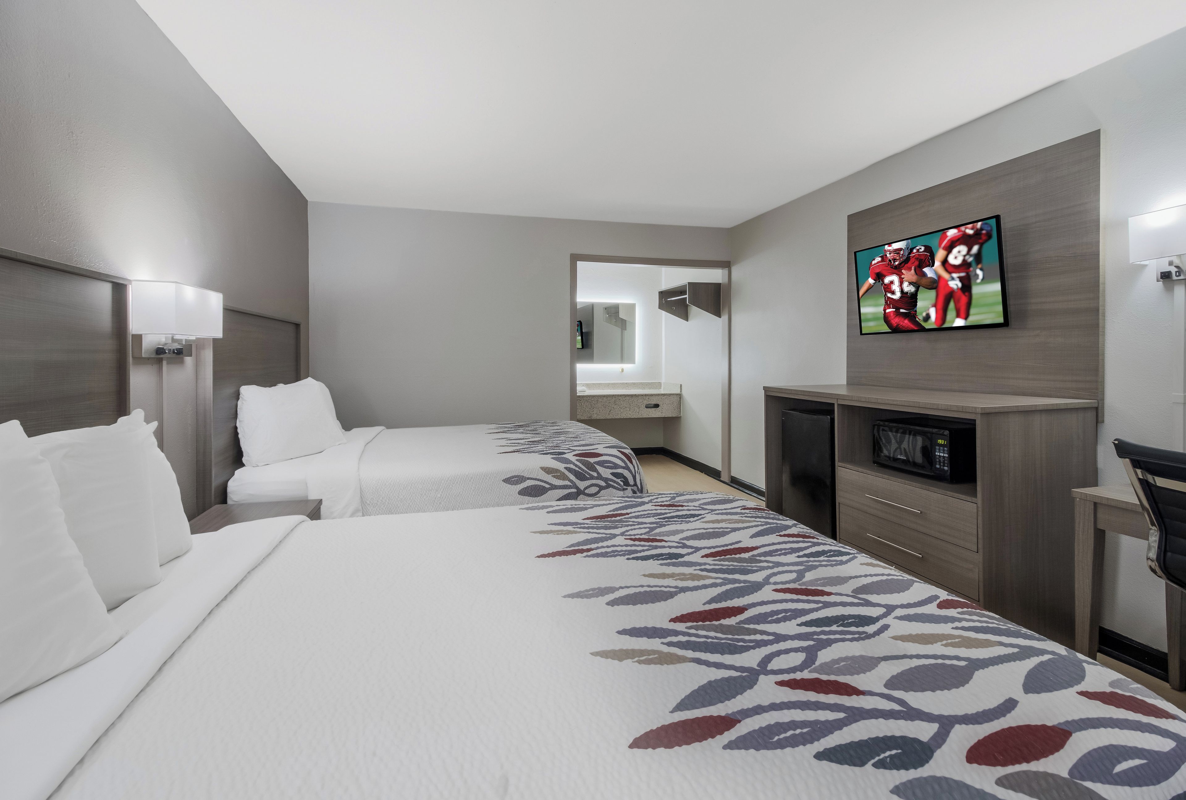 A hotel room with two beds, a television, a microwave, and a small desk.