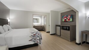 A hotel room with a bed, a TV mounted on the wall, a small refrigerator, and a desk. - Red Roof Inn & Suites Jackson, TN (Jackson)