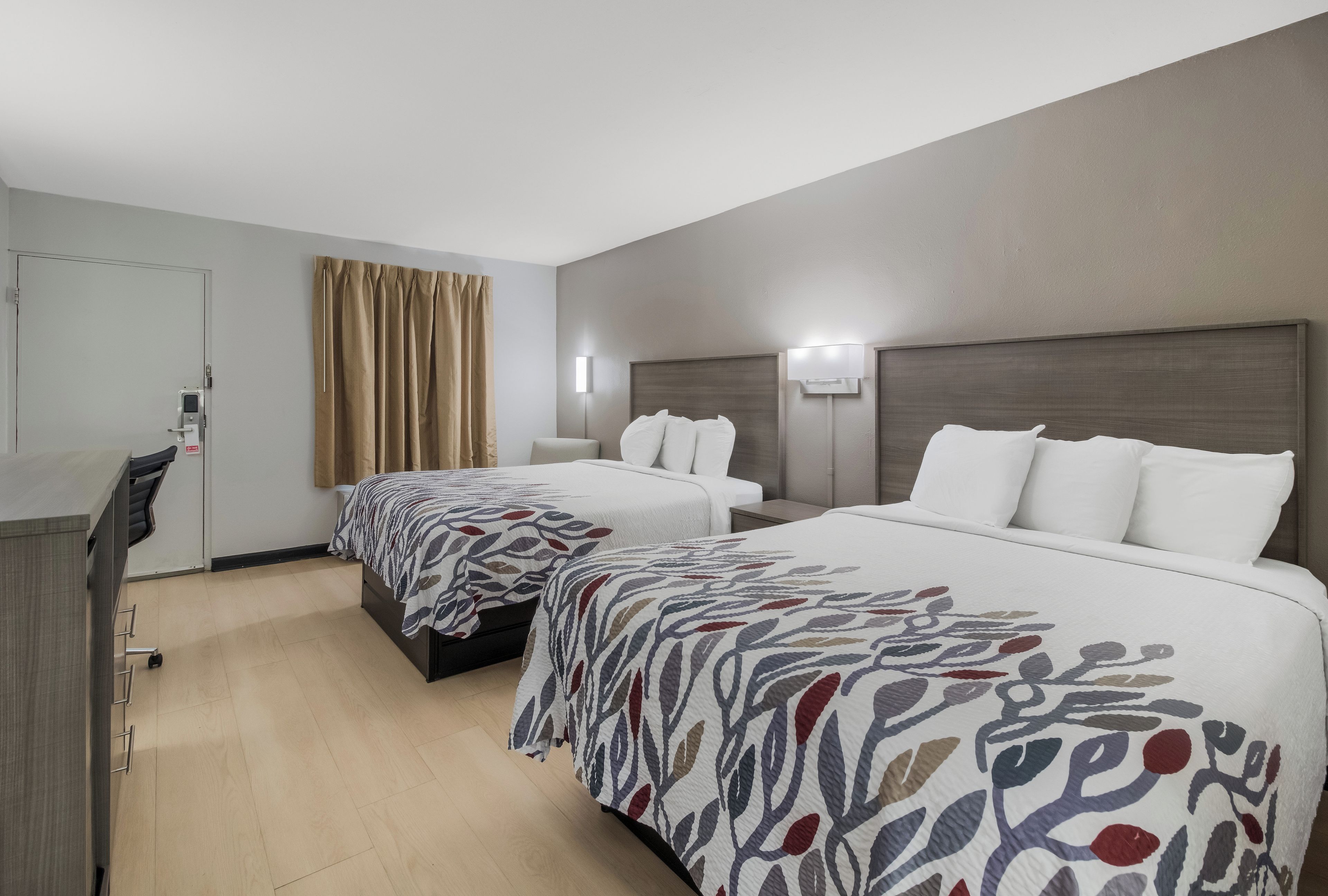 A hotel room with two beds, a desk, and a chair.