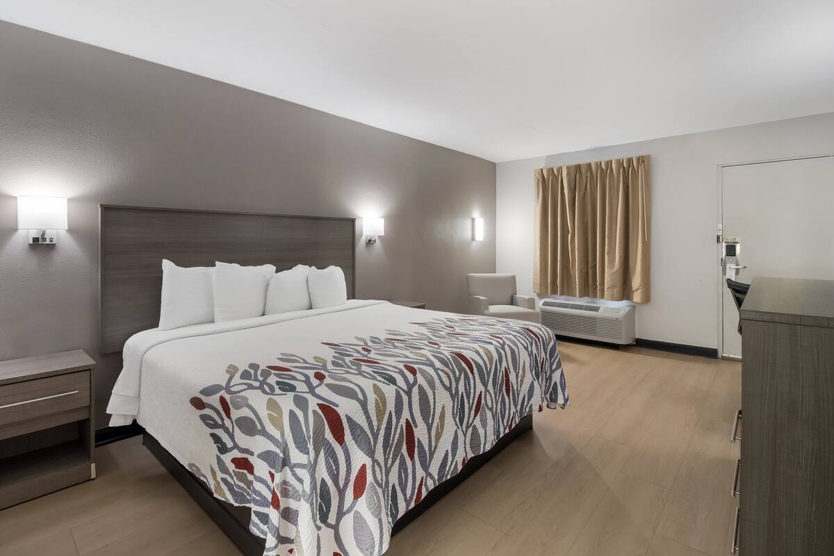 A hotel room with a large bed, bedside tables, a desk, an air conditioning unit, and a wardrobe.
