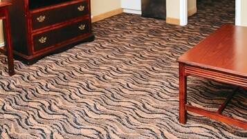 A hotel room with a wooden dresser, a television, a small kitchenette, and a patterned carpet.