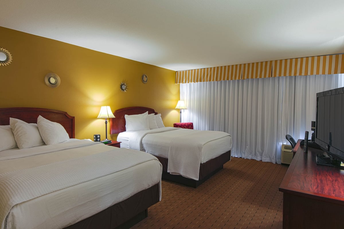 Habitación de hotel con dos camas, televisión y escritorio.