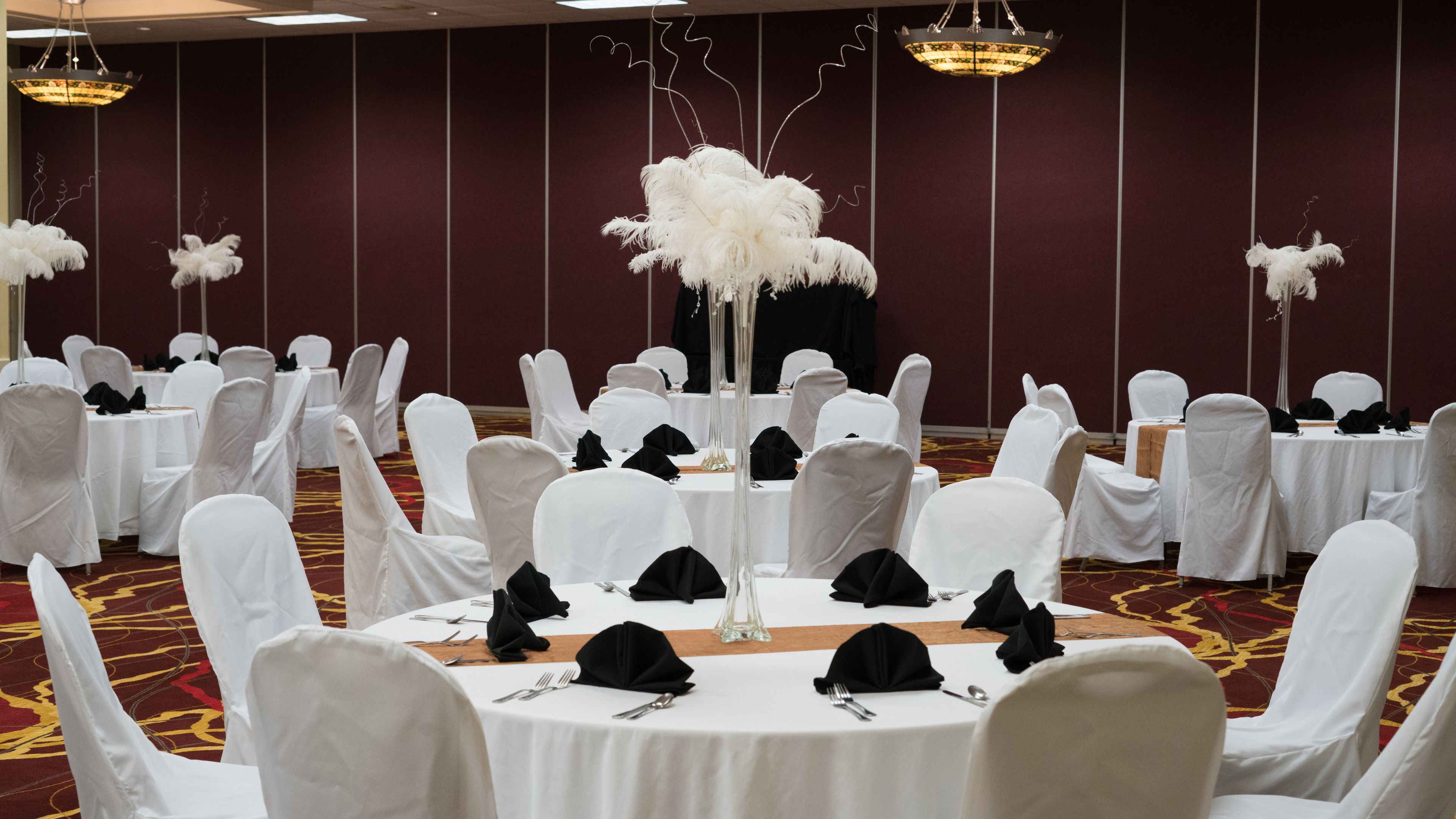 A banquet hall with round tables, white chairs, and feathered centerpieces.