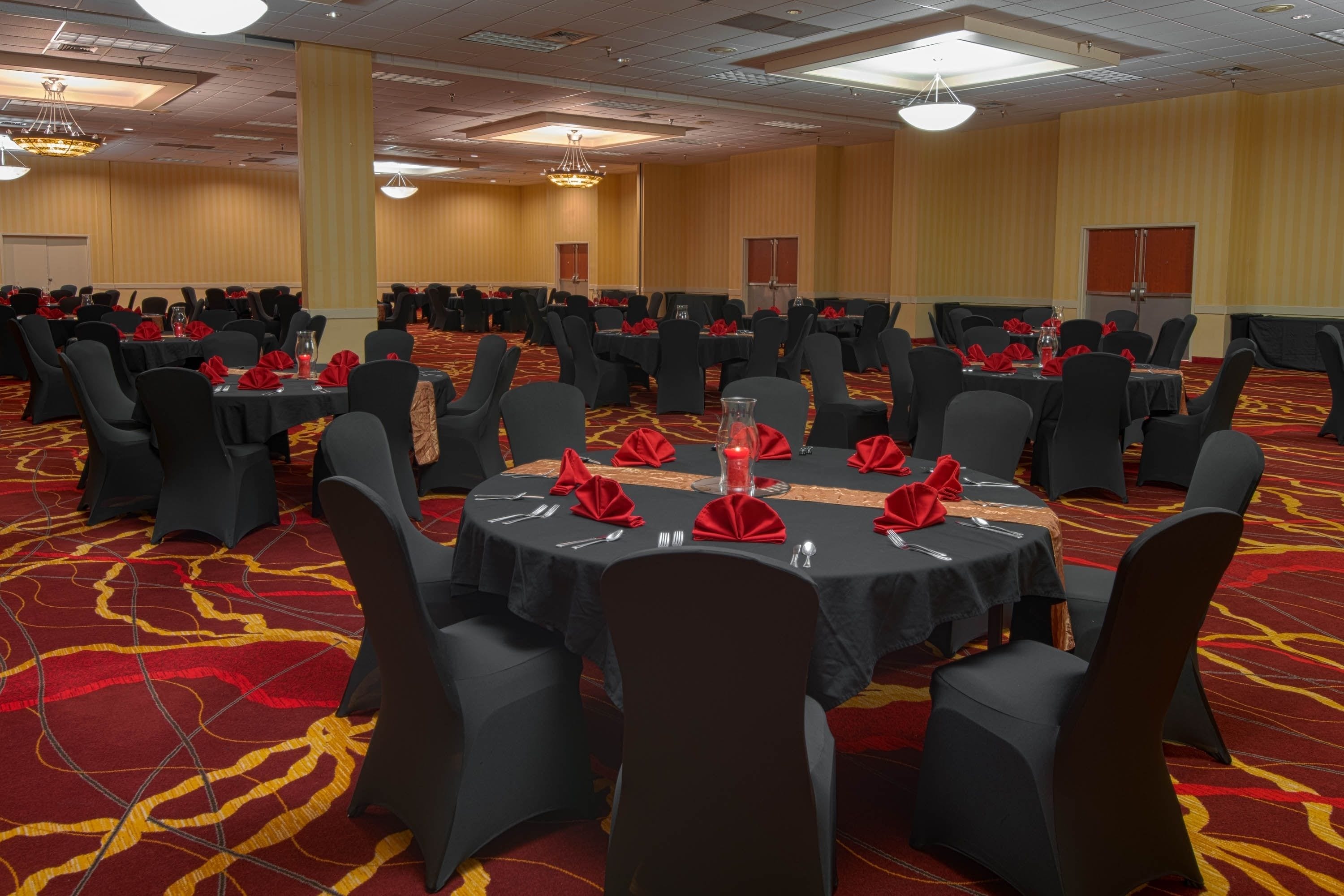 A banquet hall with round tables, black chairs, and red napkins.