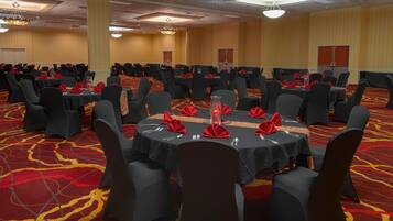Une salle de banquet avec des tables rondes, des chaises noires et des serviettes rouges.