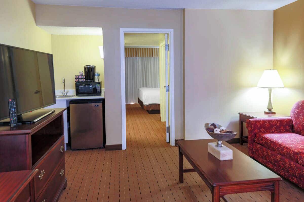 Habitación de hotel con televisión, kitchenette, cama y sofá rojo.
