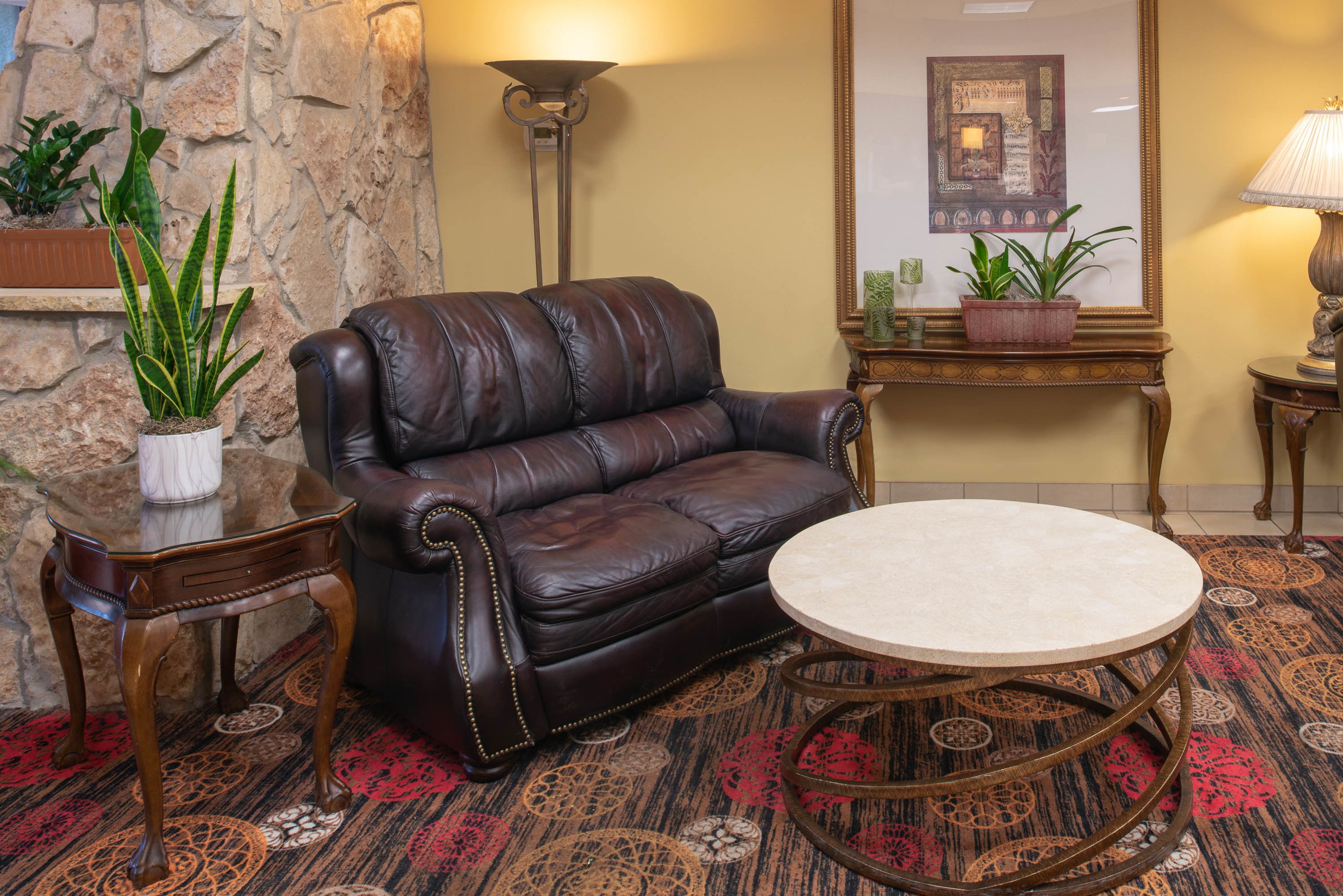 A leather sofa, a round coffee table, and a stone wall in a room with patterned carpet.