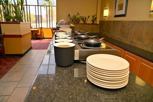 A buffet setup with various food stations, a seating area with chairs and a table, and a tiled floor.