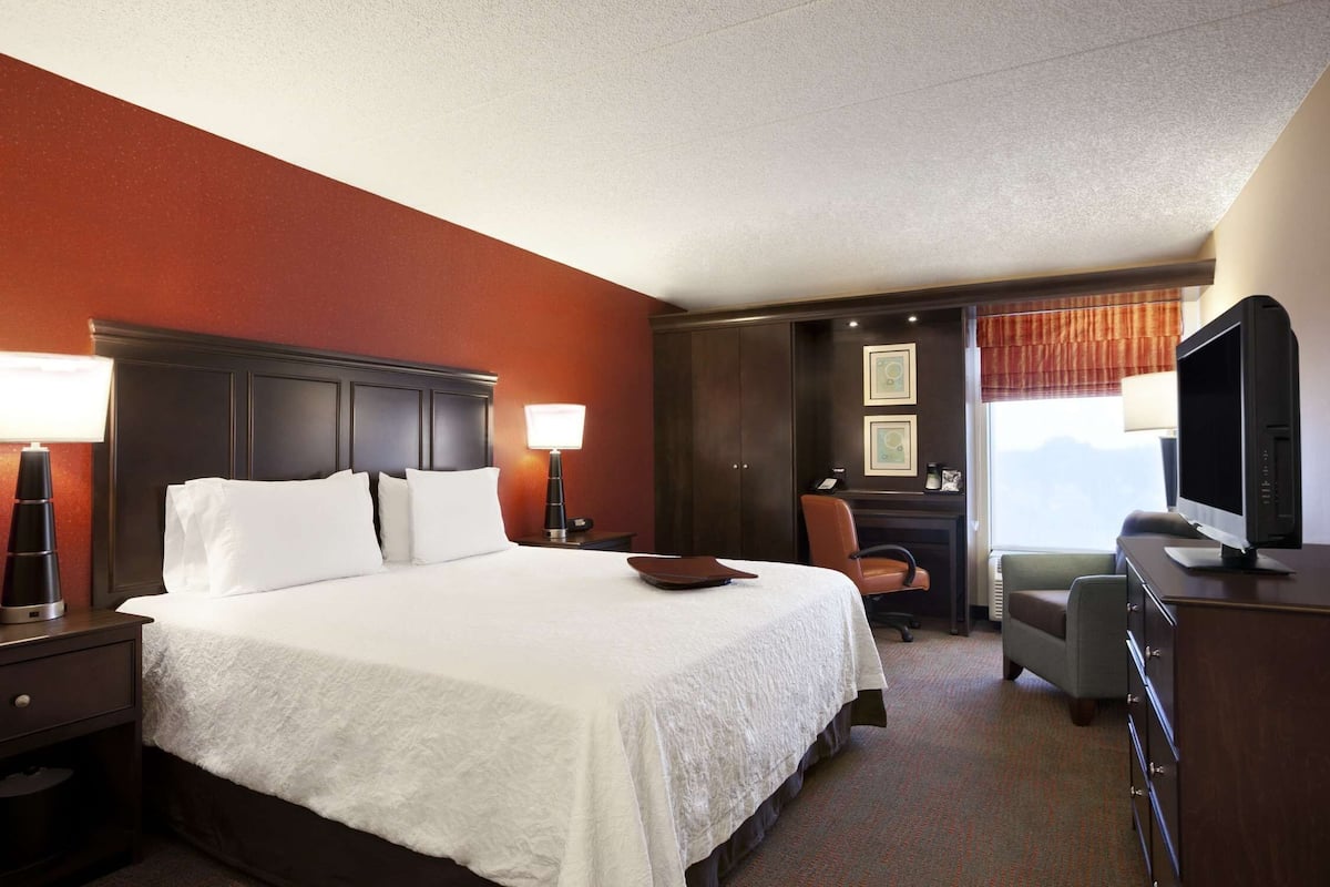 A hotel room with a large bed, a desk, a chair, a television, and a window with a view.