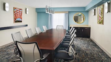 Un salón de conferencias con una larga mesa, sillas, piso alfombrado y una pared azul decorativa.