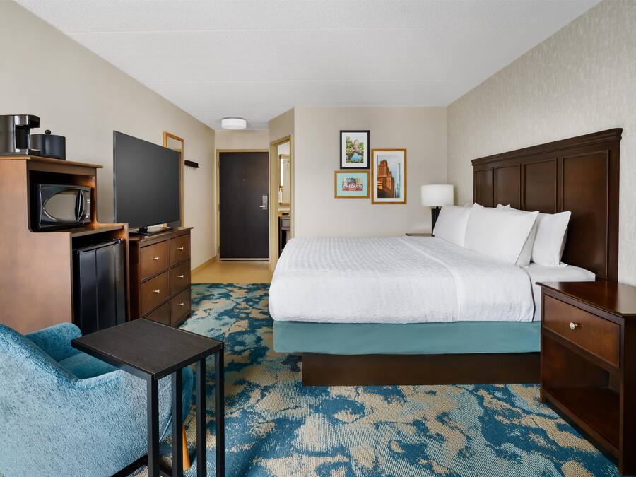 Une chambre d’hôtel équipée d’un lit, d’un bureau, d’une chaise, d’une télévision, d’un four à micro-ondes et d’une commode.