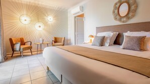 A hotel room with a large bed, two chairs, a small table, a mirror, and a ceiling light fixture. - Hôtel la Magnaneraie (Villeneuve-les-Avignon)