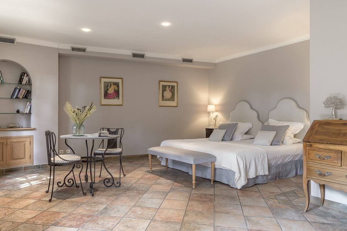 A bedroom with a bed, bedside table, lamp, and a small round table with chairs.