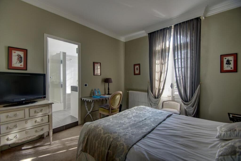 Een hotelkamer met een bed, een televisie, een bureau met stoel en een raam met gordijnen.