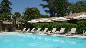 A swimming pool with lounge chairs and umbrellas, surrounded by greenery and trees. - Hôtel la Magnaneraie (Villeneuve-les-Avignon)