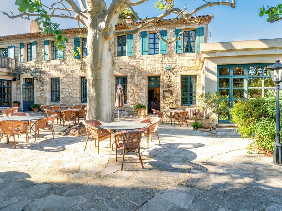 Un patio con suelo de piedra, mobiliario exterior y un edificio de paredes de piedra y contraventanas azules.