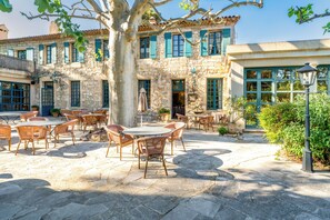 Un patio con suelo de piedra, mobiliario exterior y un edificio de paredes de piedra y contraventanas azules.
