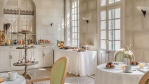 A breakfast setting with a table set for two, a buffet with pastries and drinks, and a view of the city through large windows. - Hôtel la Magnaneraie (Villeneuve-les-Avignon)