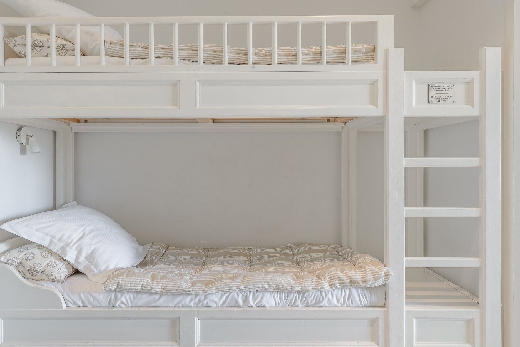 A bunk bed with a lower bunk and a top bunk, both with white bedding and a striped pillow.