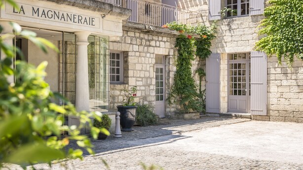 A stone building with a sign reading "LA MAGNANERAI." It features a cobblestone courtyard, potted plants, and a balcony with white shutters. - Hôtel la Magnaneraie (Villeneuve-les-Avignon)