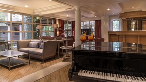 A spacious living room with a grand piano, comfortable seating, and large windows offering a view of the outdoors. - Hôtel la Magnaneraie (Villeneuve-les-Avignon)