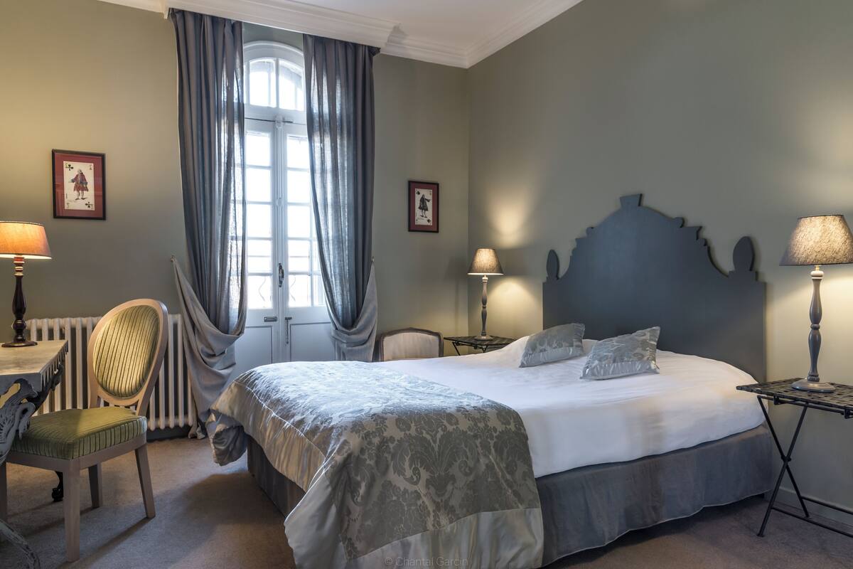 A bedroom with a large bed, a chair, a table, and a lamp.