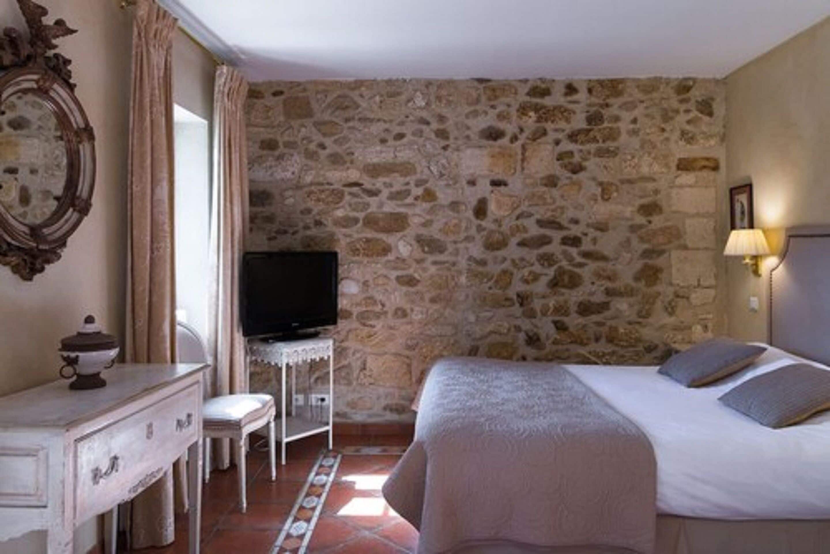 A bedroom with a stone wall, a bed, a TV, a dresser, and a chair.