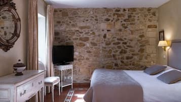 A bedroom with a stone wall, a bed, a TV, a dresser, and a chair.