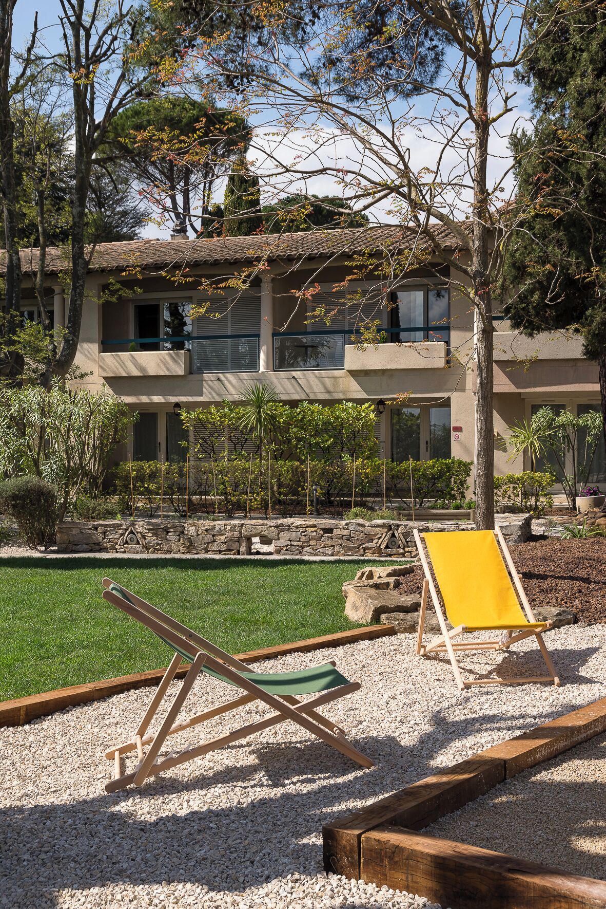 A modern building with a stone facade, a green lawn, and a yellow lounge chair.