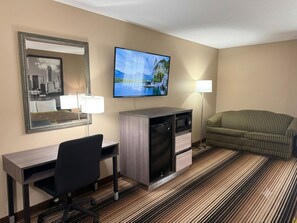 A hotel room with a desk, chair, television, microwave, and a sofa. - Super 8 by Wyndham Harrison OH (Harrison)