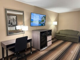 Habitación de hotel con escritorio, silla, televisor, microondas y sofá.