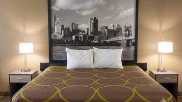 A hotel room with a bed, two bedside lamps, a framed cityscape picture, and a nightstand with a drawer.