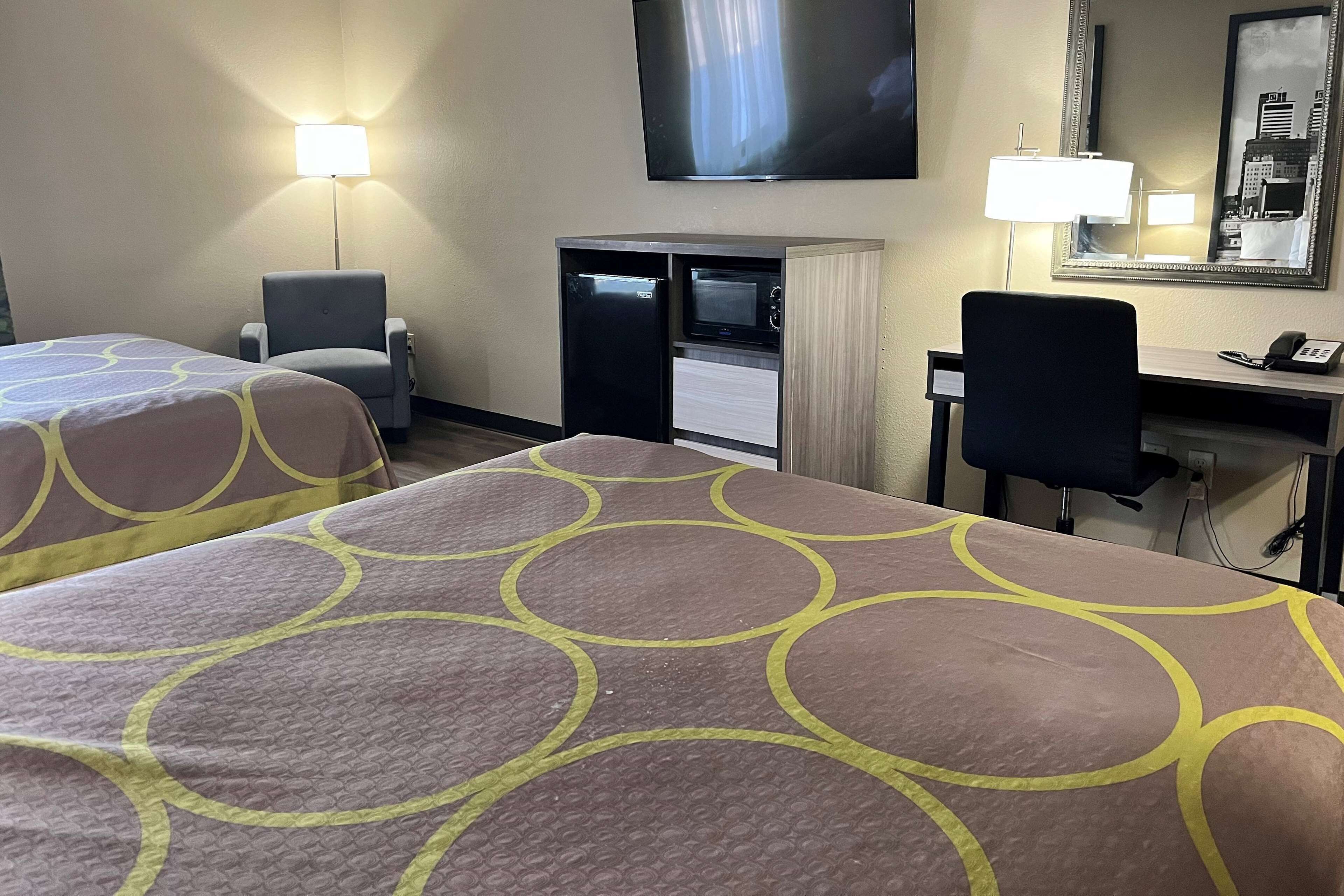 Habitación de hotel con dos camas, un escritorio, una silla, un televisor y un espejo.