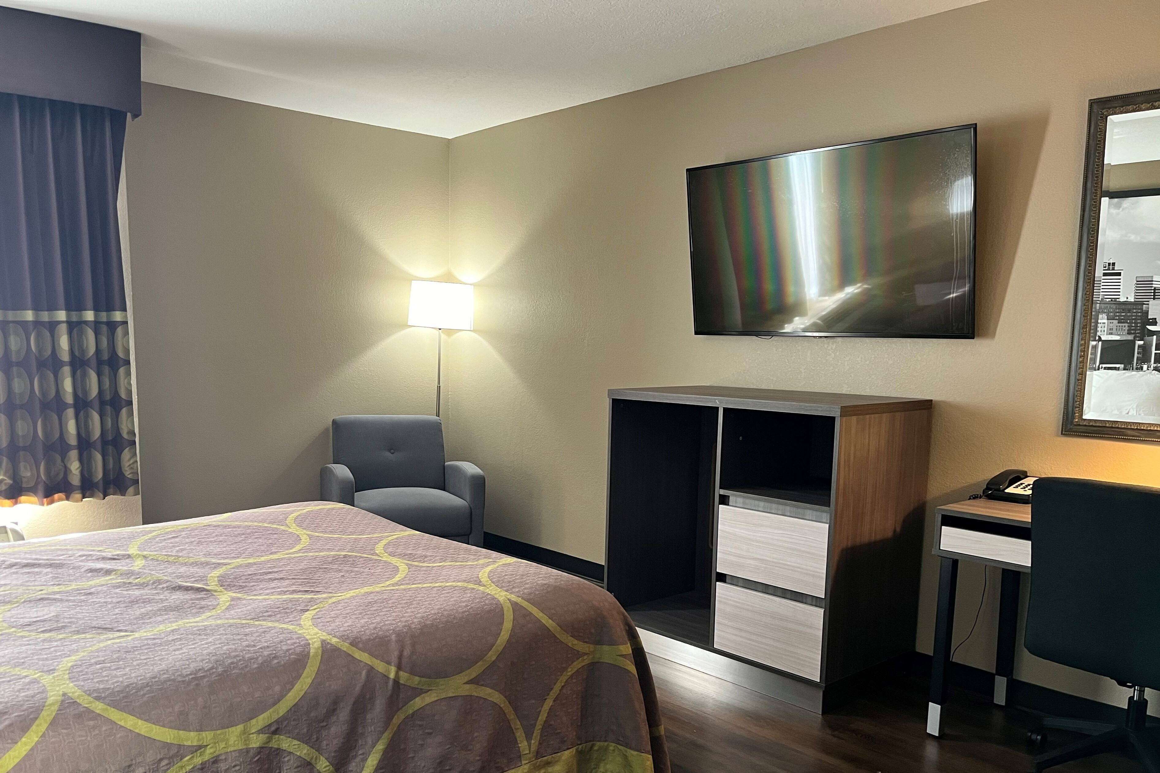 A hotel room with a bed, a desk, a chair, a TV, and a lamp.