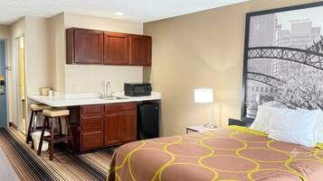 A hotel room with a bed, a kitchenette, a cityscape view, and a door.